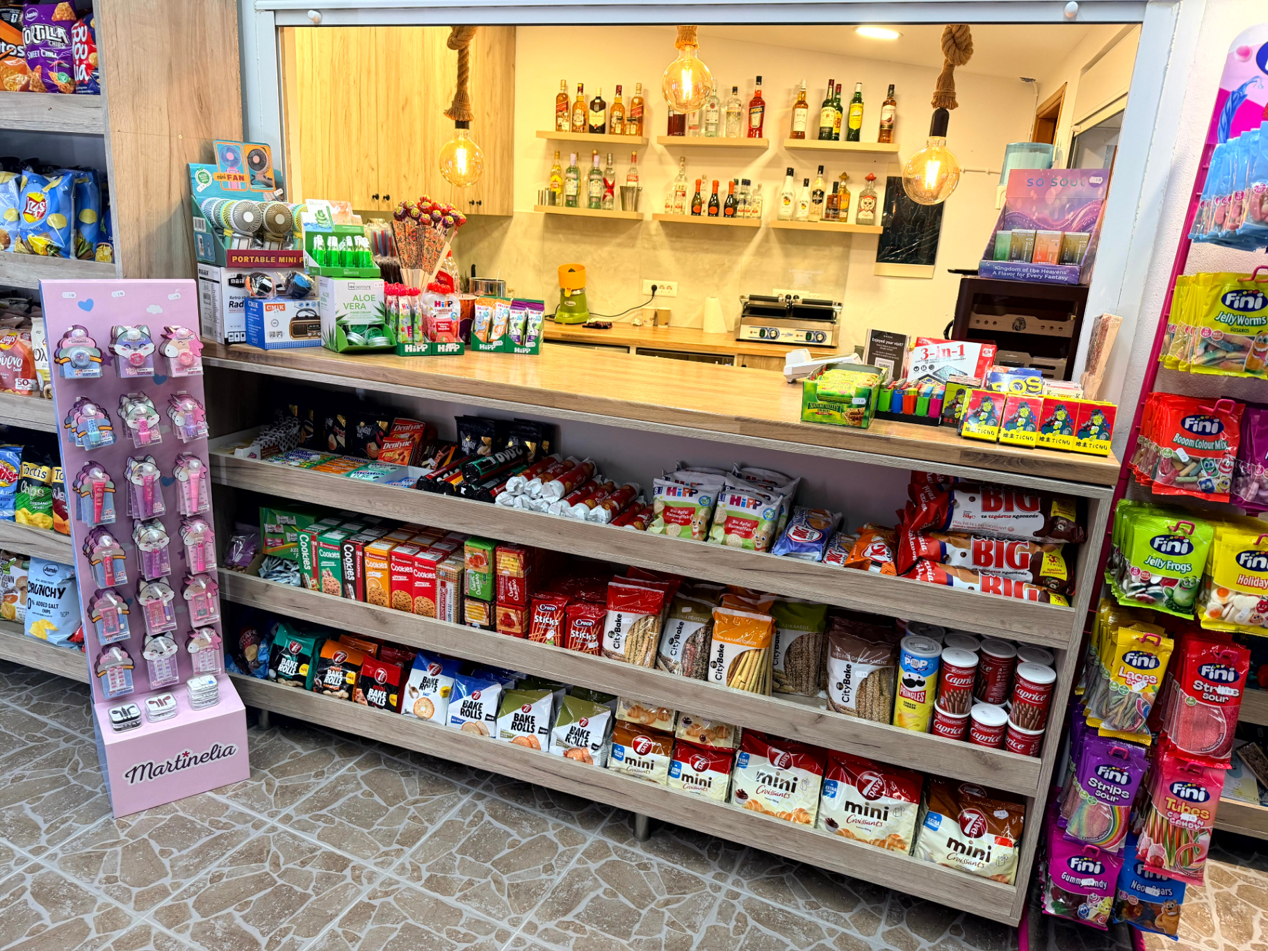 Πάγκος με snacks, γλυκά, mini croissants και ράφια με ποτά στο βάθος
