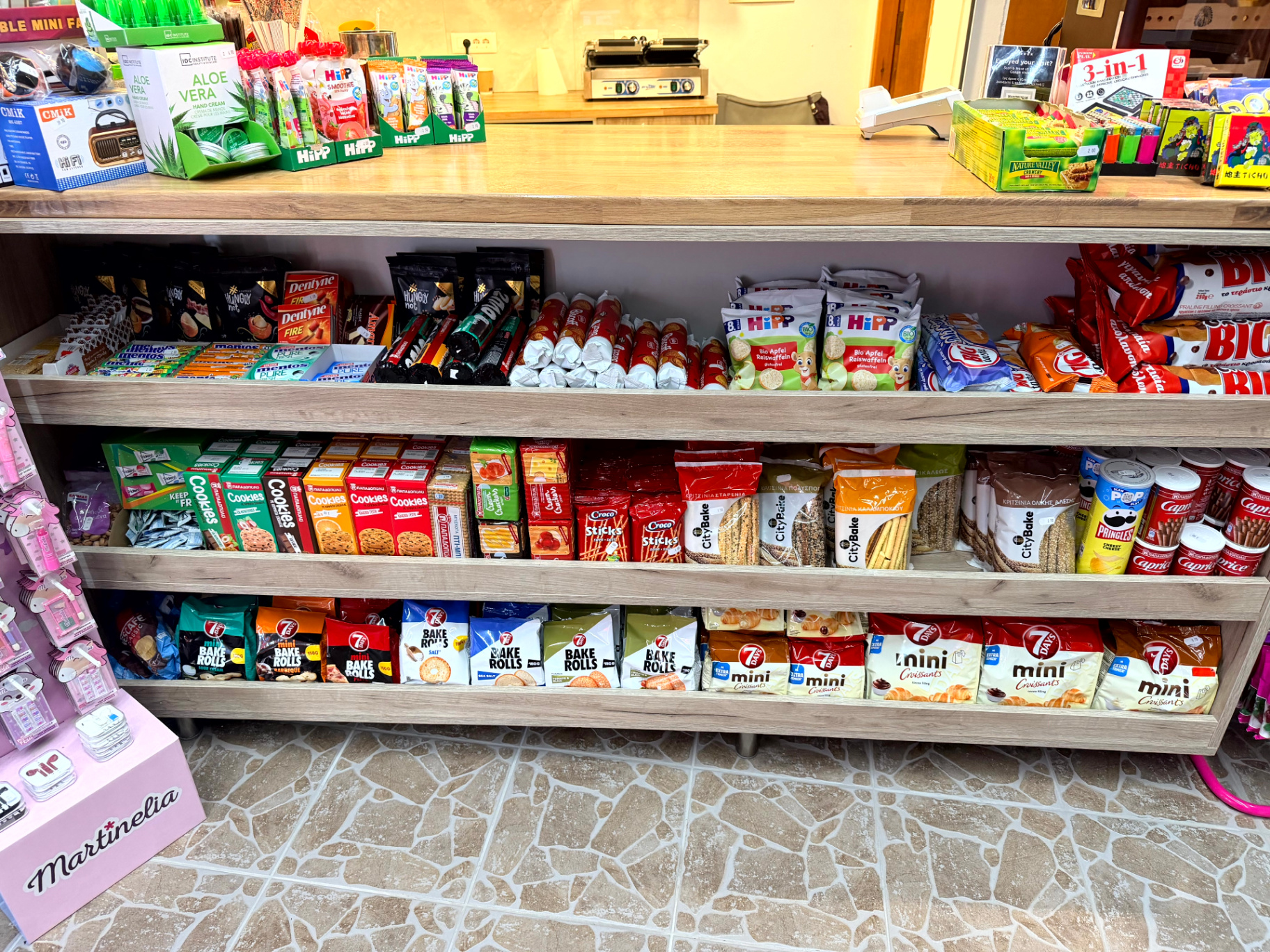 Ράφια με μπισκότα, cookies, 7Days mini croissants, Pringles και snacks κάτω από τον πάγκο